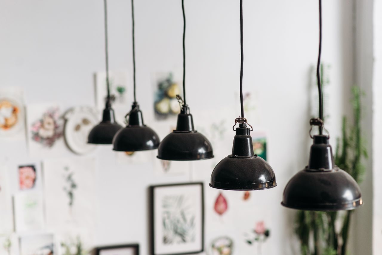 A row of black pendant lamps hanging in a creatively decorated indoor space with artwork.